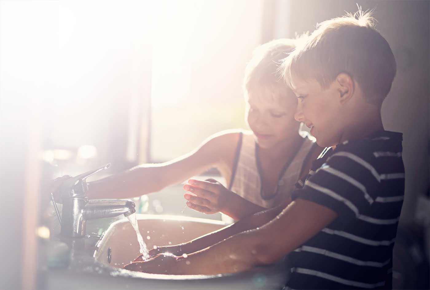 Two young boys washing their hands in a sink.