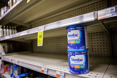 Mostly empty grocery store shelves with only two containers of Similac baby formula sitting on them.