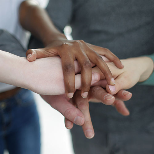 Hands of ethnic diversity are joined in the center of a group of people.