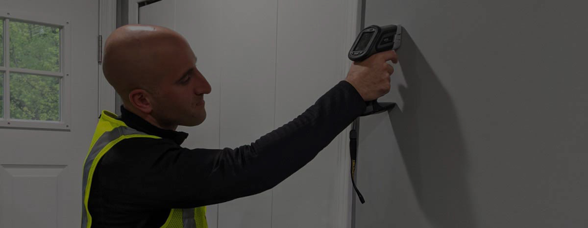 A lead inspector checks paint on a wall using a hand-held lead paint analyzer.